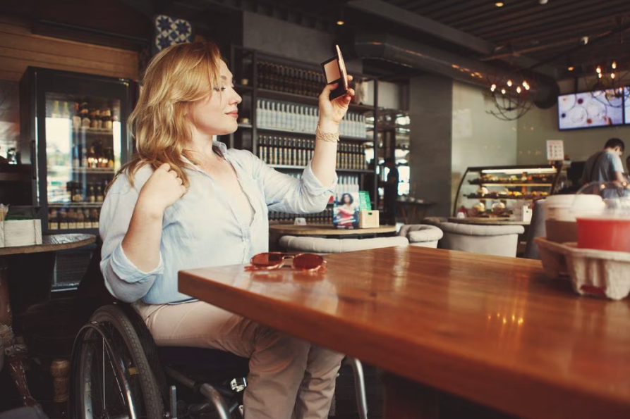 A disabled woman in wheelchair uses her phone to take a selfie picture inside a restaurant.
