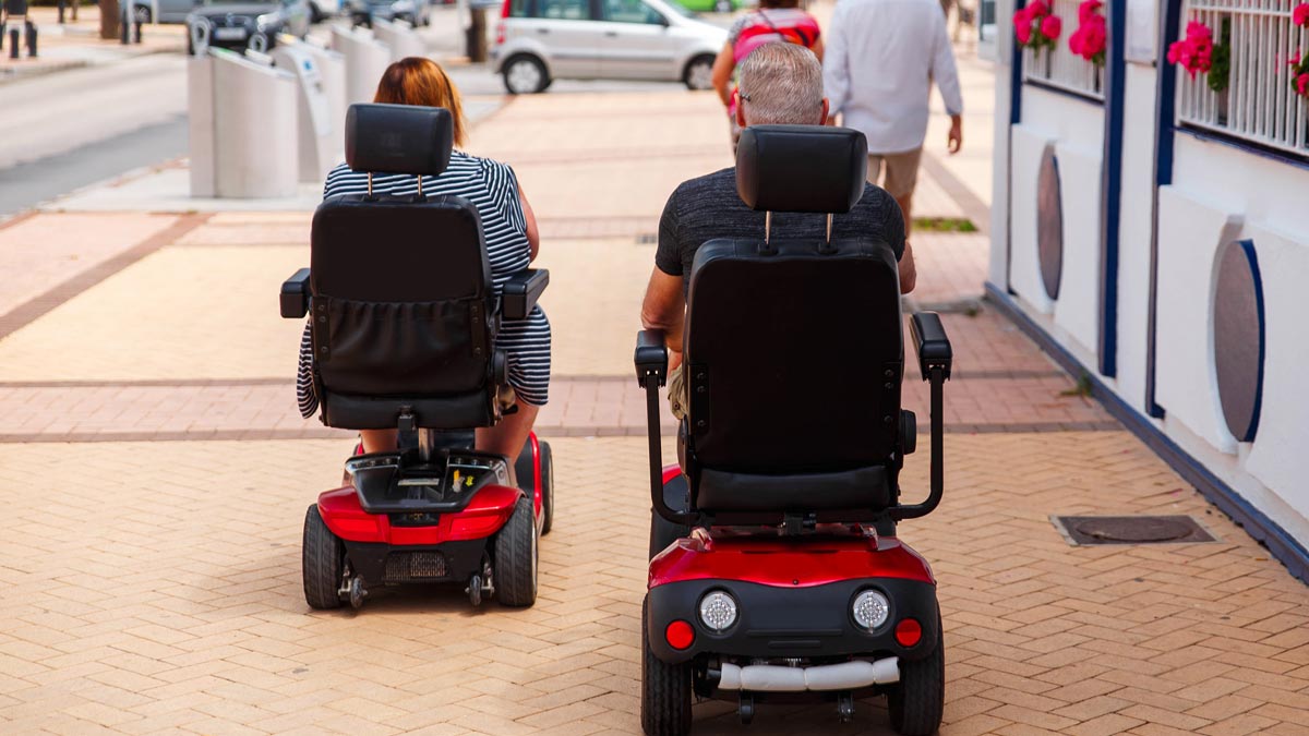 Two power wheelchair users using the sidewalk on a city street