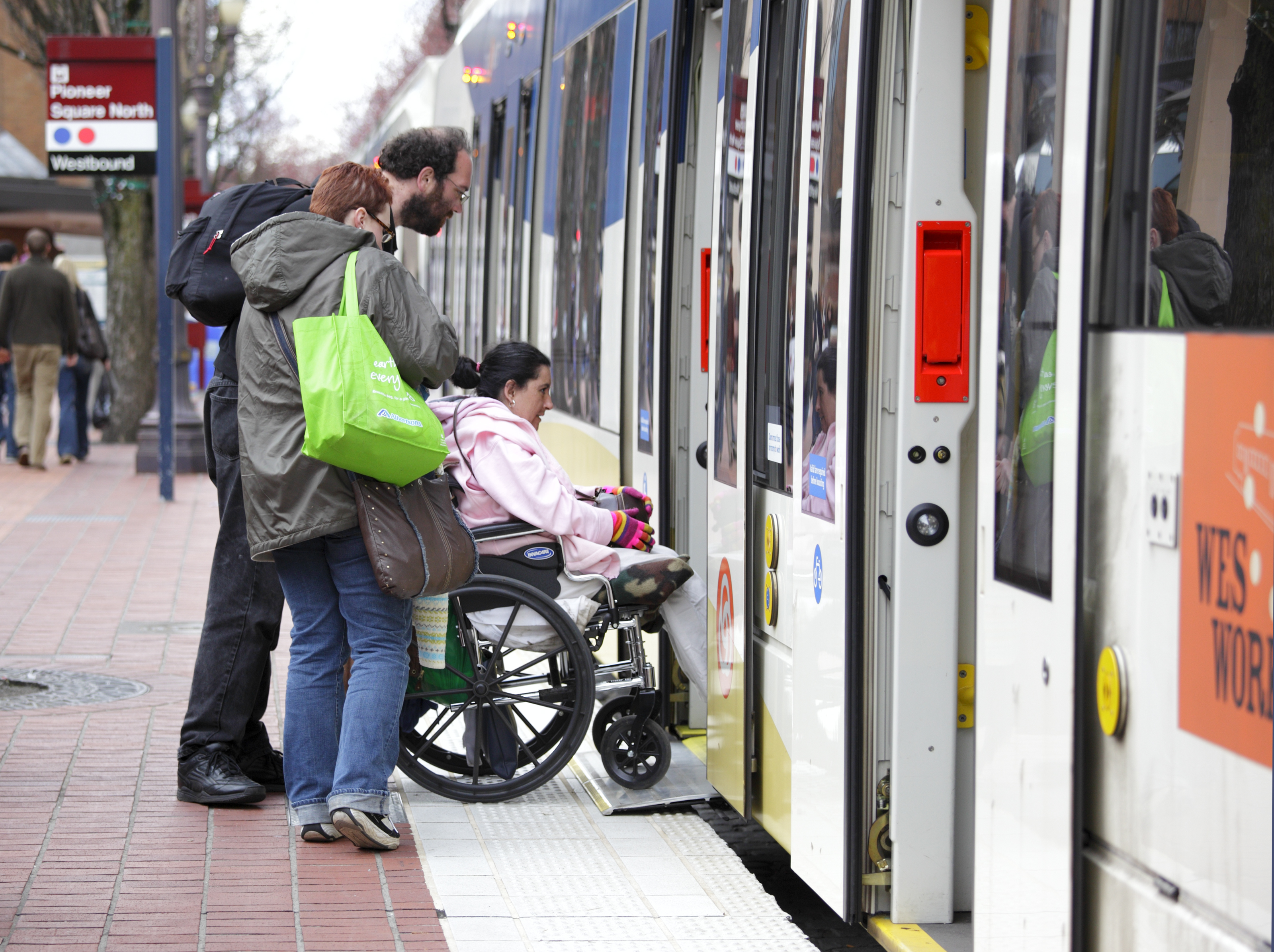 Family boarding train pushing child in a wheelchair.  Accessible train station.