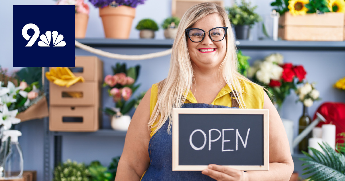 business owner stands in flower shop holding sign that says 