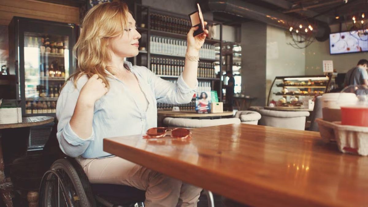 A disabled woman in wheelchair uses her phone to take a selfie picture inside a restaurant.