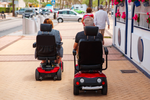 Two power wheelchair users using the sidewalk on a city street.