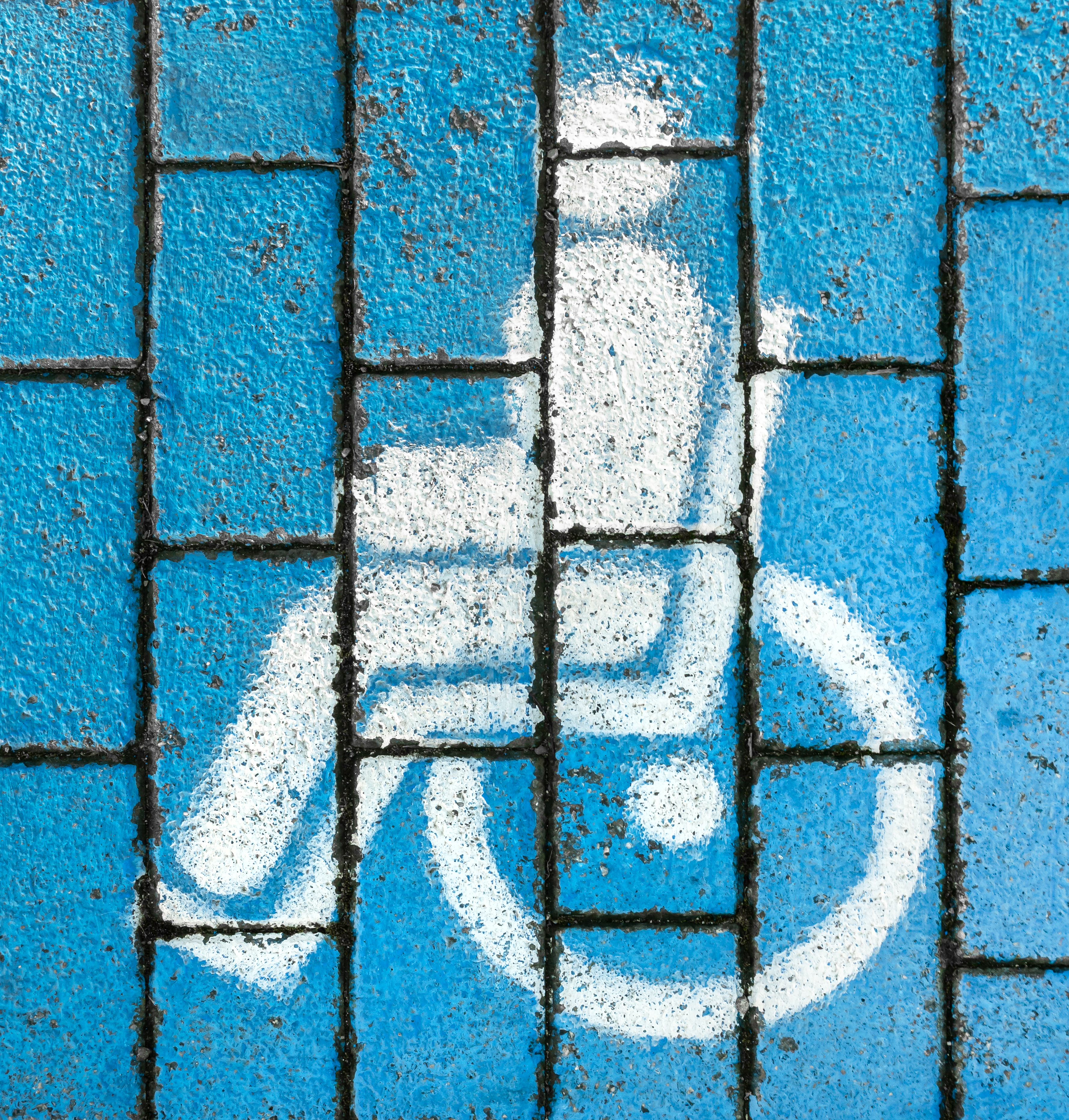 A wheelchair symbol spray painted on blue bricks.