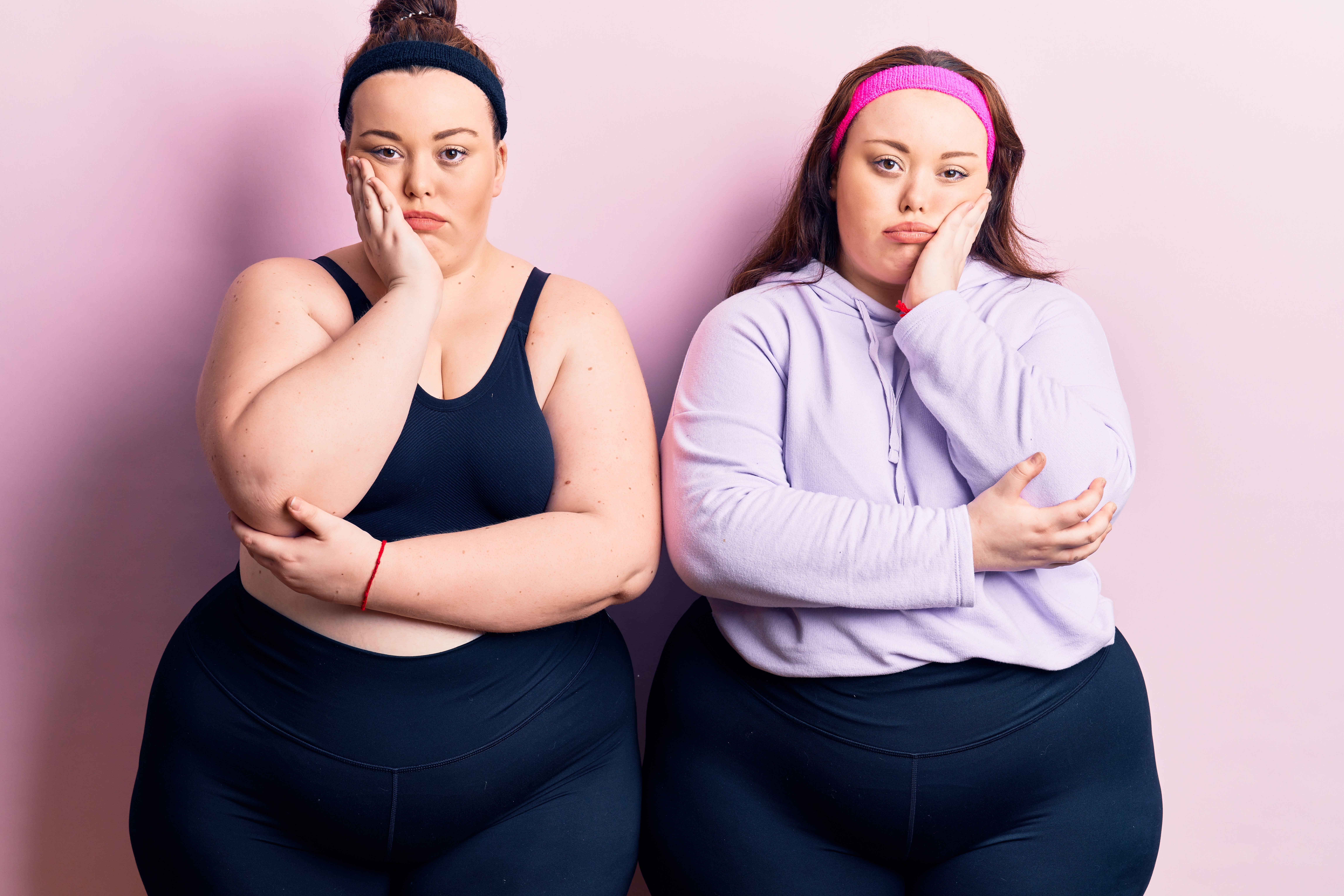 Two plus-size women in athletic clothing with tired expressions.