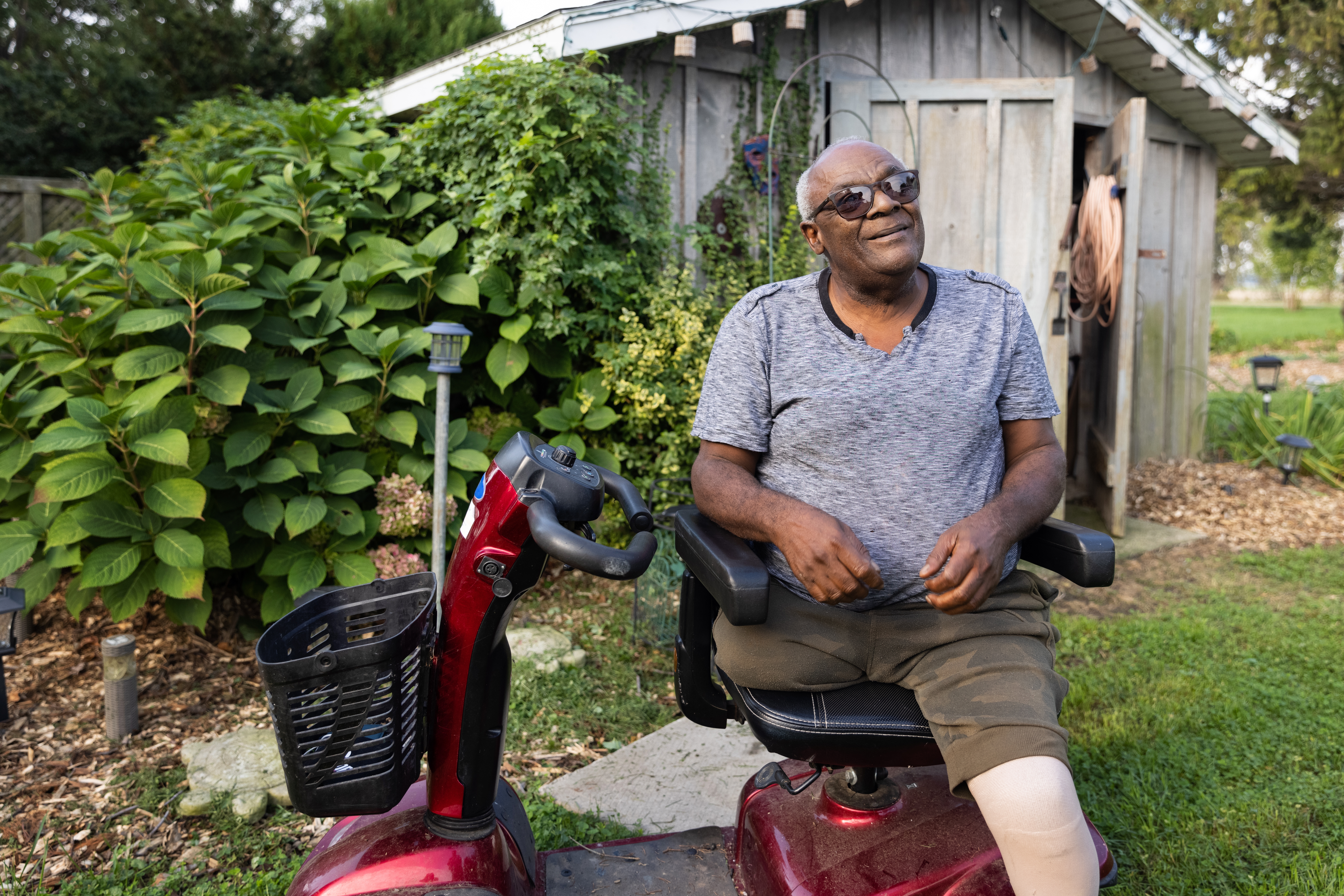 An older man sitting in a motorized scooter enjoying the sunshine in his garden.