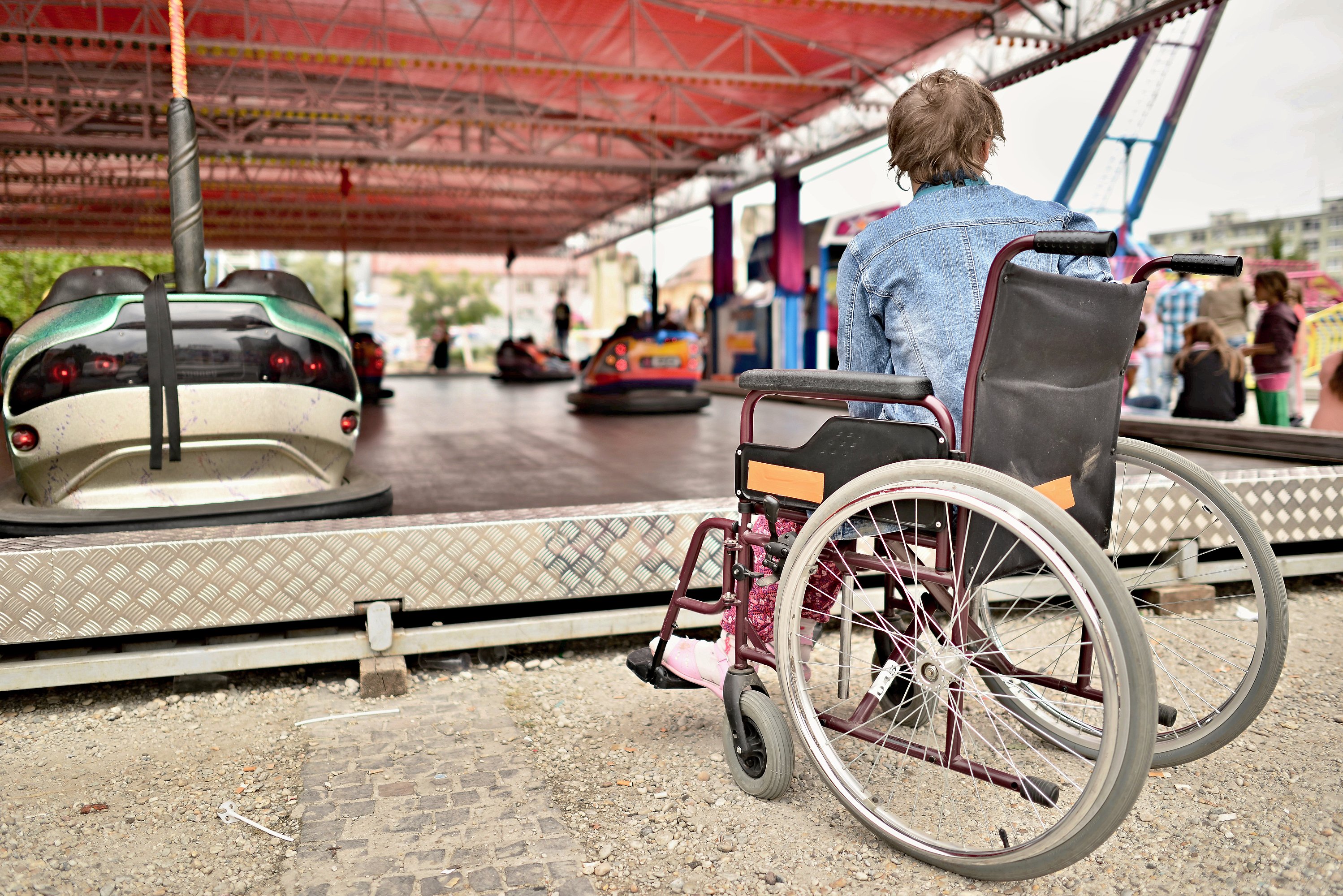 Woman faces away from camera in a wheelchair looking at bumper car ride.