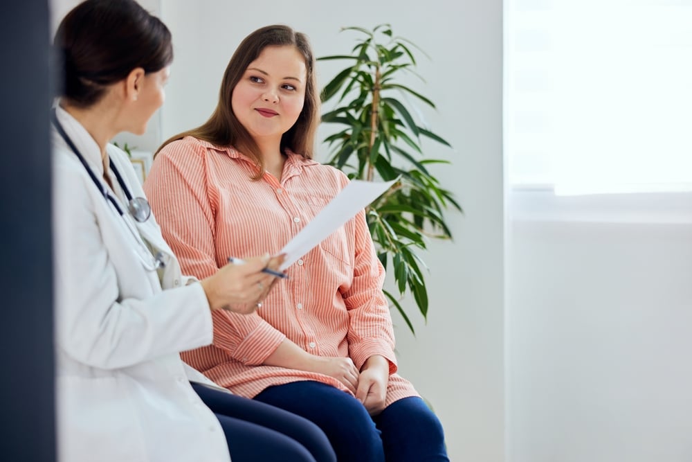 A woman sitting beside a doctor reading paperwork to her.